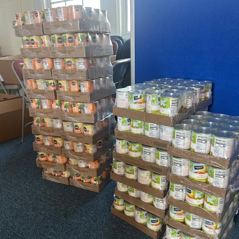 FD Food Closet 1 Tall stacks of canned goods on cardboard pallets in a room, ready for distribution or donation.